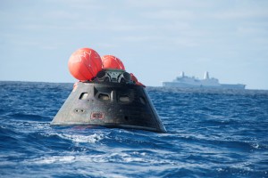 Crew module after splash down in the Pacific Ocean with the Crew Module Uprighting System bags deployed and the USS Anchorage in the background